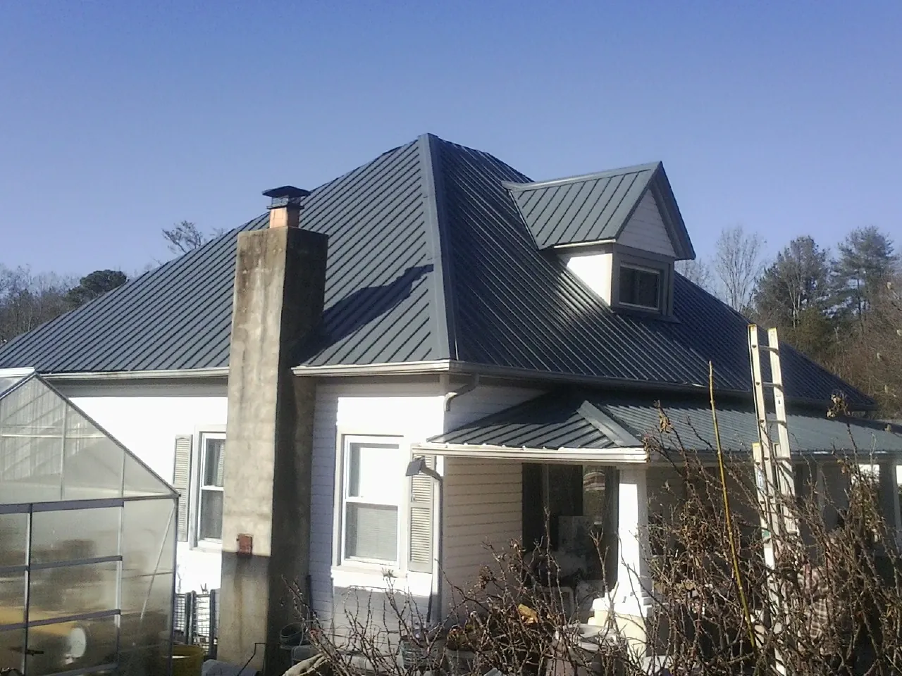 Dark blue standing seam metal roof on a white farmhouse with dormer — Slate & Tile Roof Repair by Roofing Brothers in West Yellowstone