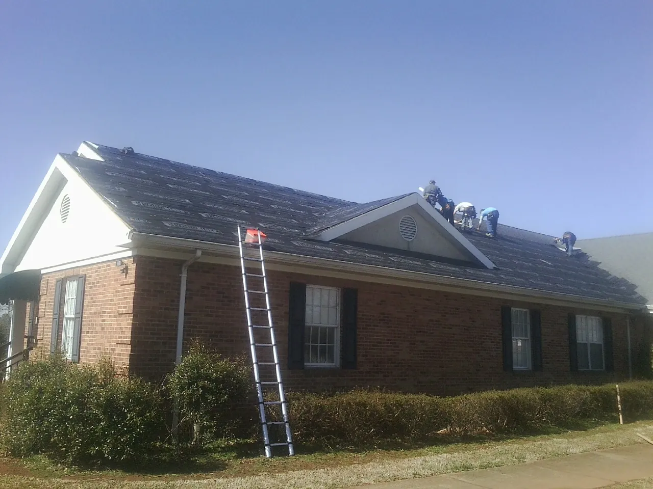 Crew tearing shingles off a brick ranch roof with a ladder set — Metal Roof Repair work by our crew in West Yellowstone