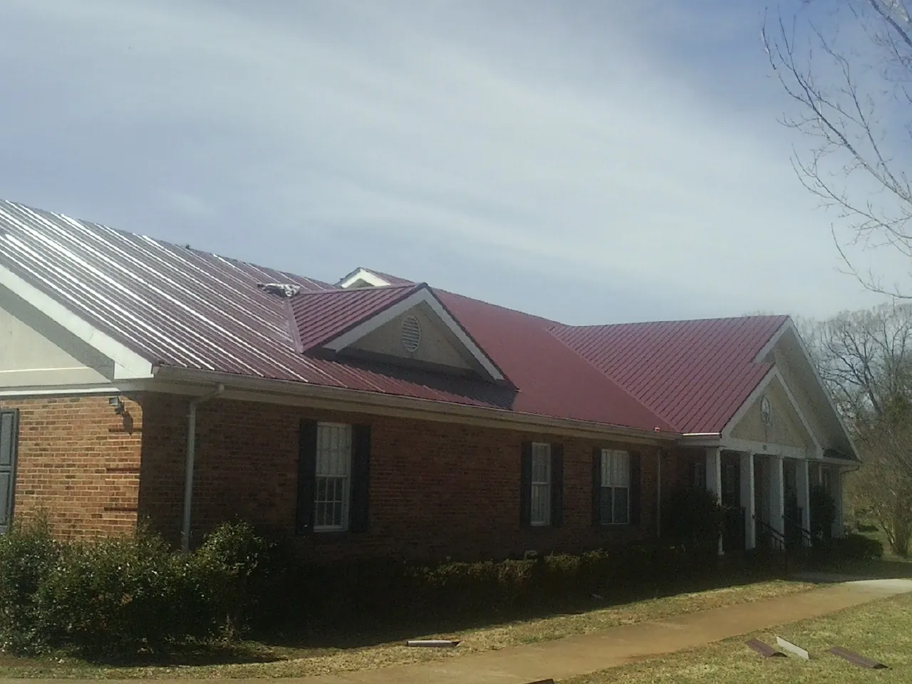 Red metal roof with gabled entries on a long brick building, from a Hail Damage Roof Repair job in West Yellowstone