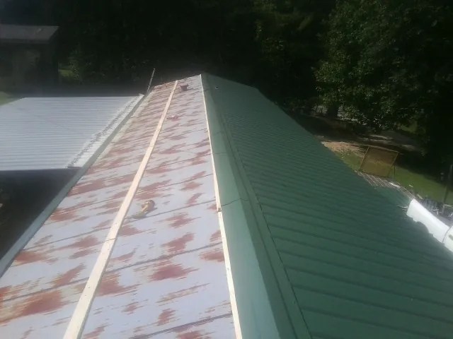 Old rusted panels beside newly installed green metal roofing — Wind Damage Roof Repair by Roofing Brothers in West Yellowstone