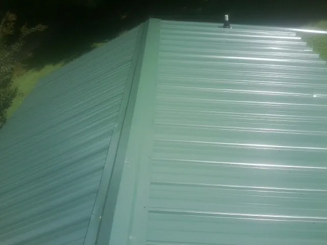 New green metal panels meeting at the ridge of a roof — Flat Roof Repair work by our crew in West Yellowstone