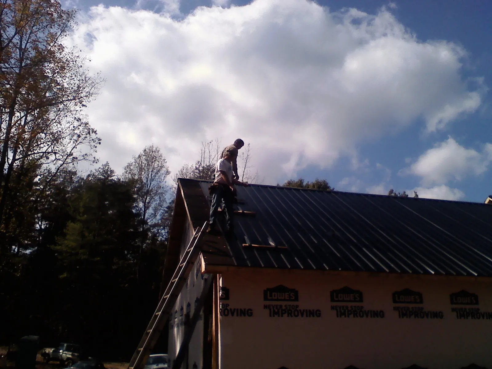 Roofer fastening dark metal panels high against a cloudy sky, from a Roof Inspection job in West Yellowstone