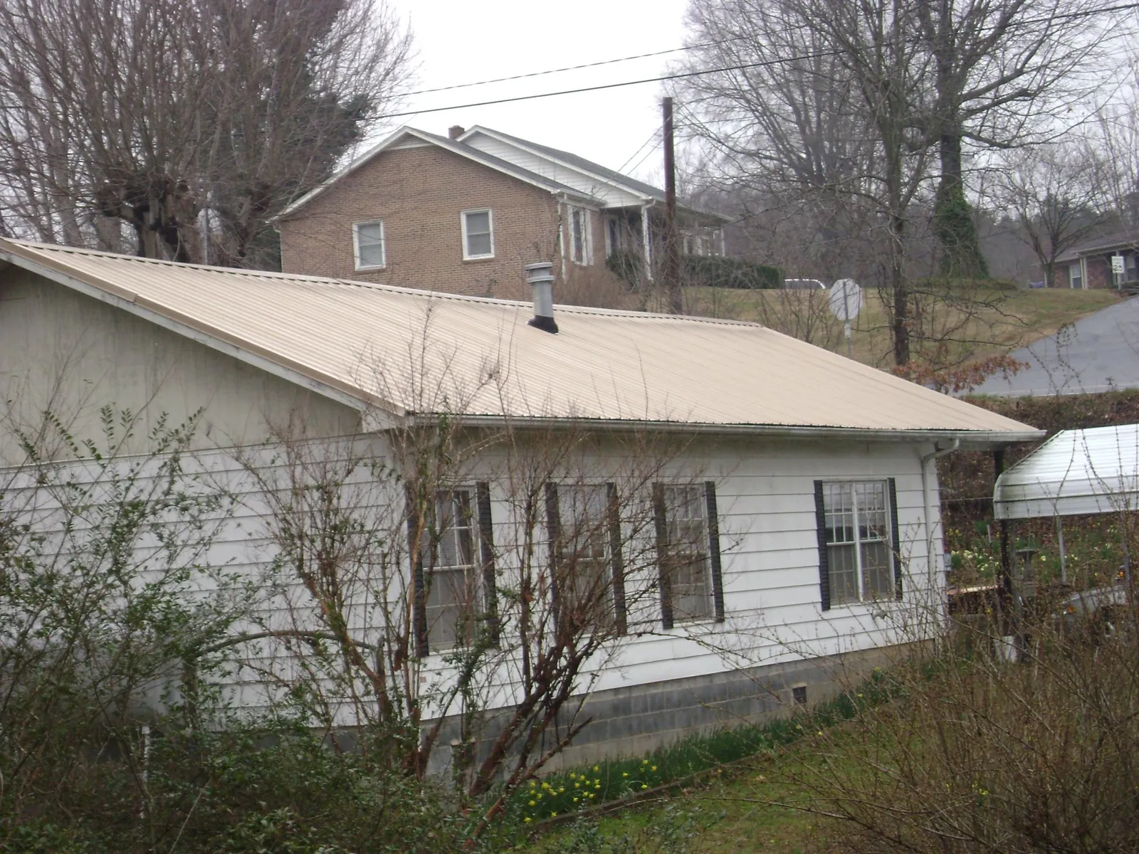 Tan metal roof on a white sided house set into a hillside — Commercial Roofing by Roofing Brothers in West Yellowstone