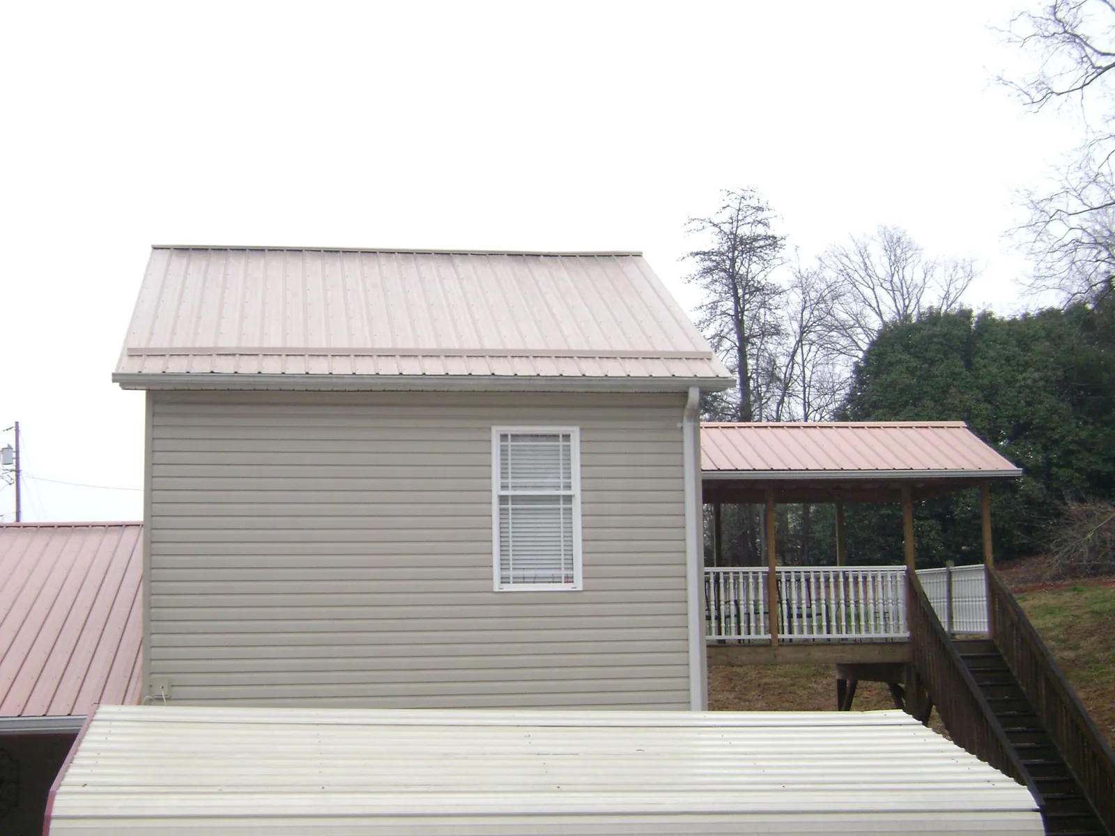 Tan metal roofs on a two story addition and attached porch, from a Roof Replacement job in West Yellowstone